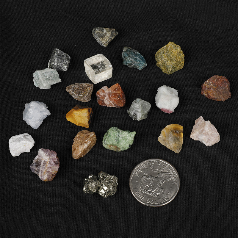 Assorted raw gemstones on a dark surface with a coin for scale.