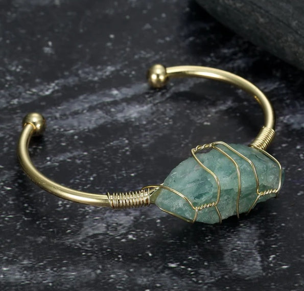 Gold bracelet with a green stone on a dark surface