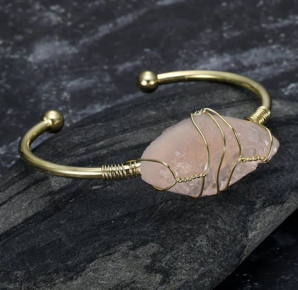 Gold bracelet with a pink stone on a dark stone surface