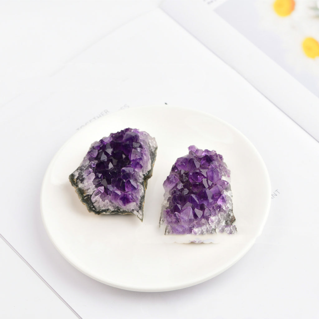 Two purple amethyst crystals on a white plate with a white background